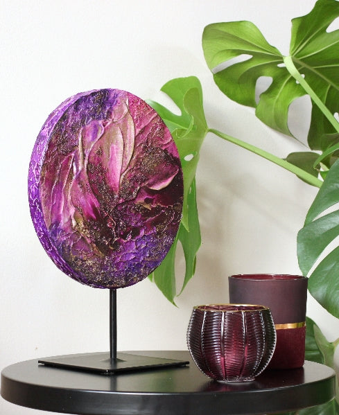 A circle pink-purple abstract painting on a sculpure pedestal.
