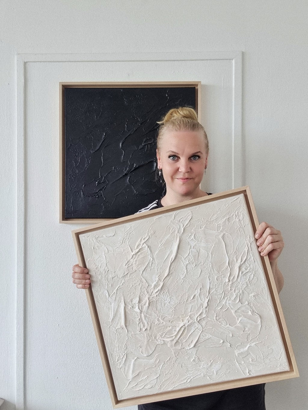 Blonde female artist holding a monochromic textured painting in the studio.